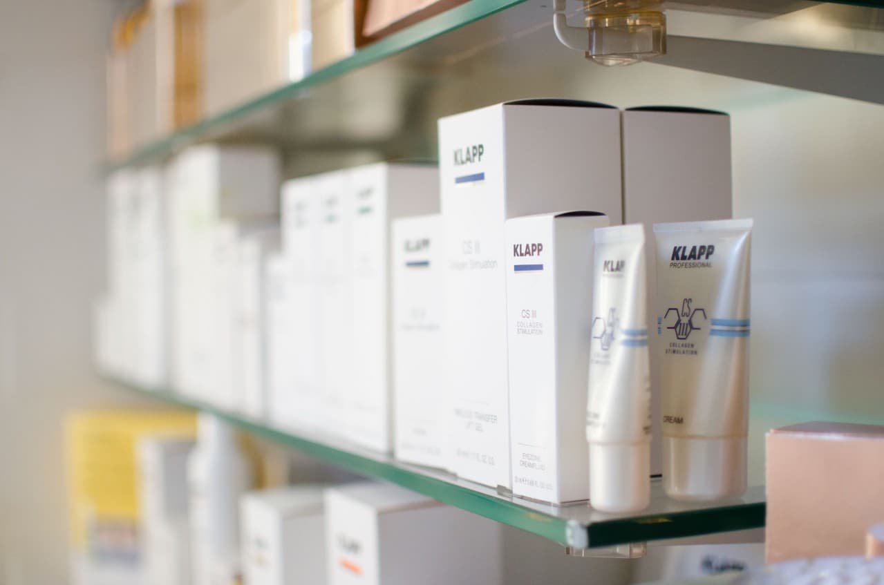 Glasregal mit weißen KLAPP-Verpackungen und Cremetuben der Linie CS III