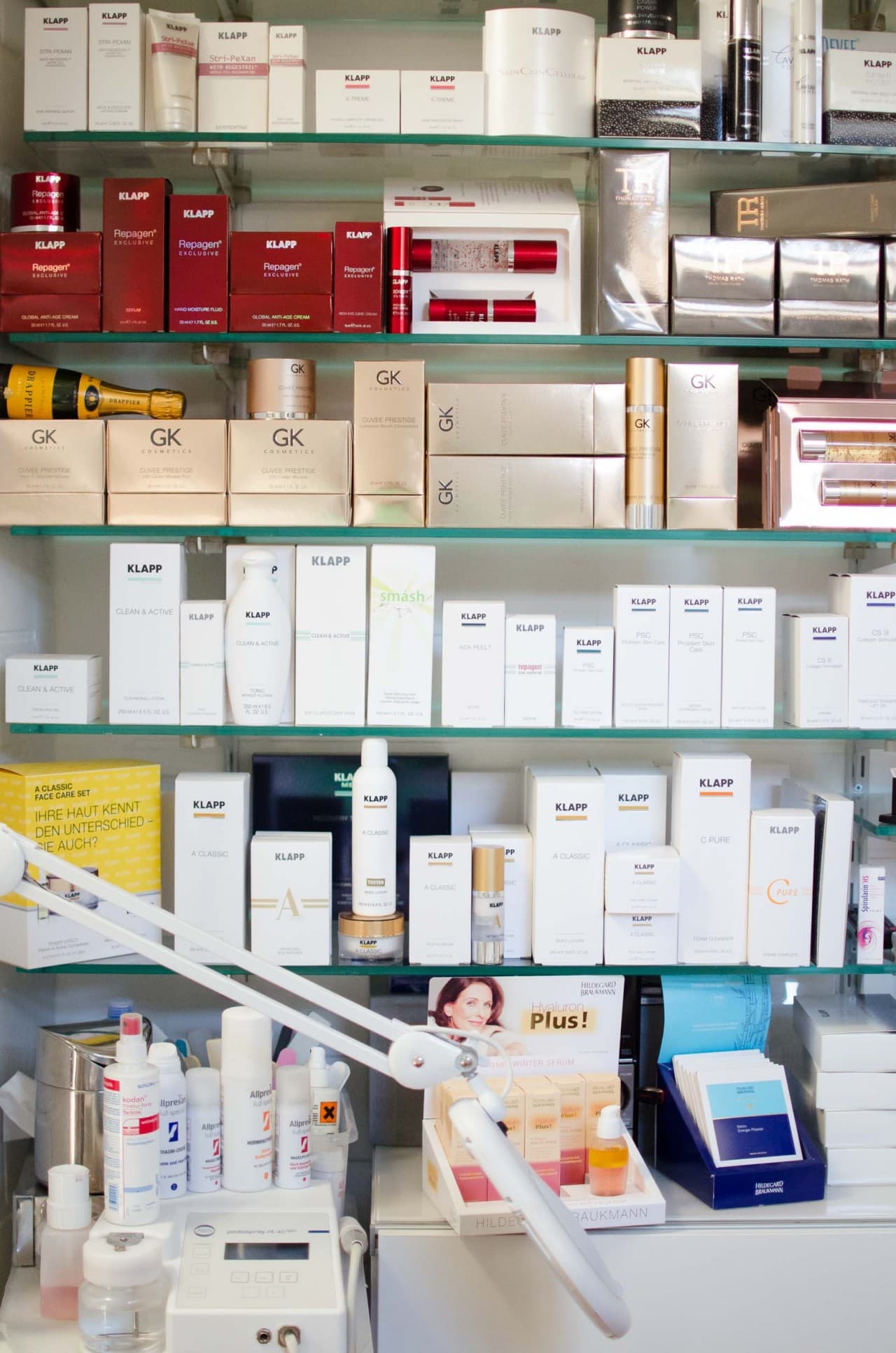 Glasregal voller Pflegeprodukte: rote und weiße KLAPP-Verpackungen, goldfarbene Schachteln weiterer Marken und ein Aufsteller von Hildegard Braukmann